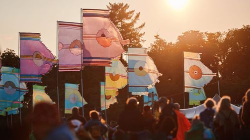 Several tall colourful festival flags at an outdoor festival on a summer evening