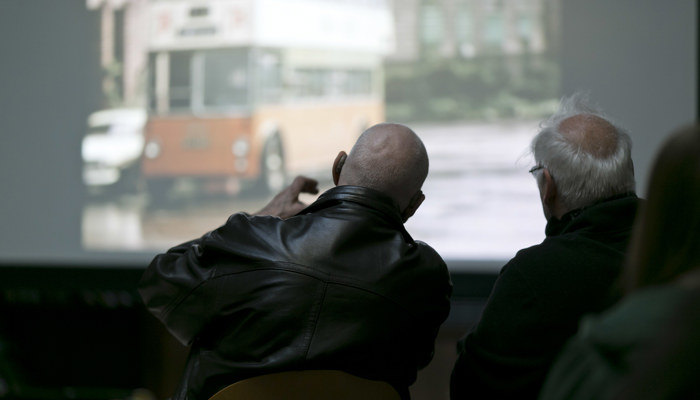 Two community member sit facing a slide show of historic images. 