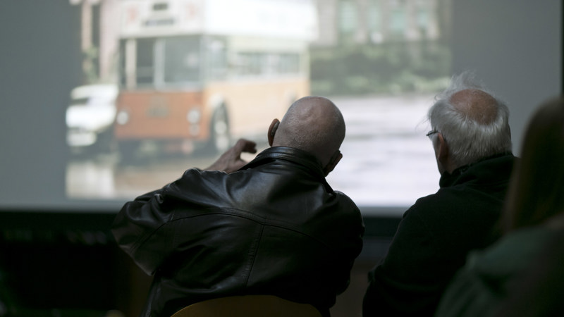 Two community member sit facing a slide show of historic images. 