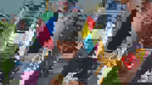 A young person wearing colourful elephant ears made of paper, smiling and sitting at a craft table in a library