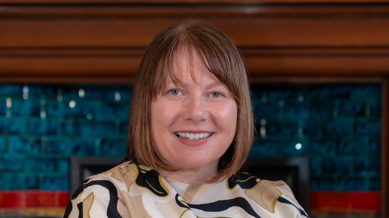 A photo of Julie Pearson sitting on a green sofa with a blue mosaic patter in the background. 