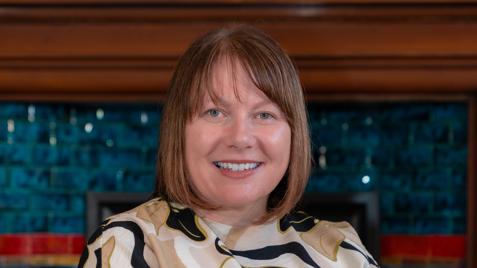 A photo of Julie Pearson sitting on a green sofa with a blue mosaic patter in the background. 