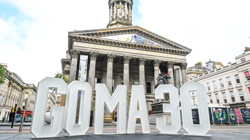 Large white letters spelling 'GOMA 30' displayed in front of Glasgow's Gallery of Modern Art, a grand neoclassical building with tall columns and a tower.