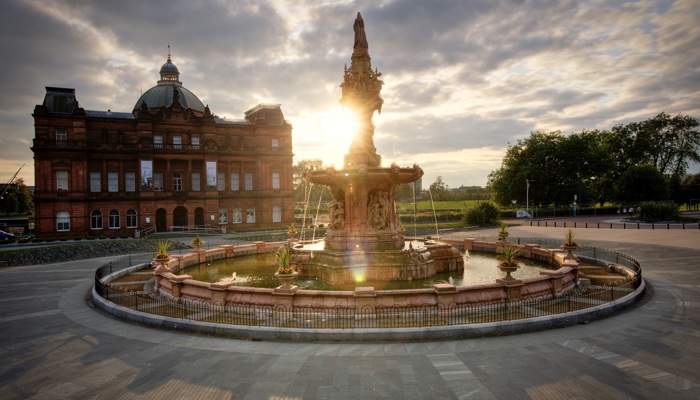 The Doulton Fountain in Glasgow in front of the People's Palace and Winter Gardens with the sun setting in the background.