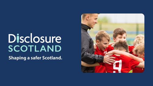 A football coach with a group of young players, all in red football kits, gathered arm in arm in a circle on a football pitch