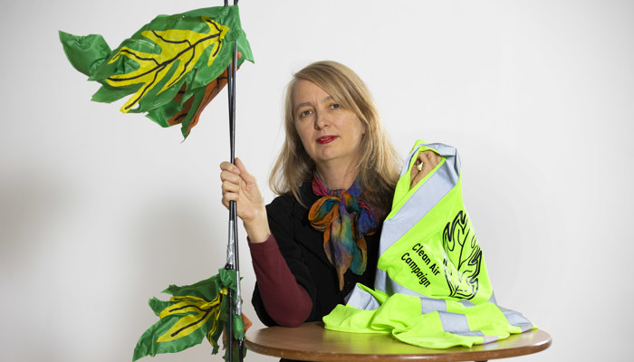 Artist Zoe Walker poses with a high vis waistcoat and leaf prop