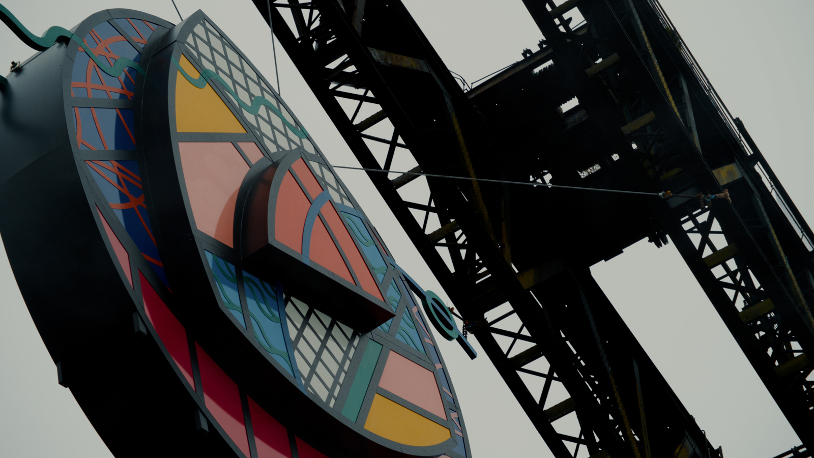 A close-up of a large circular artwork of a multicoloured rose hanging from a crane