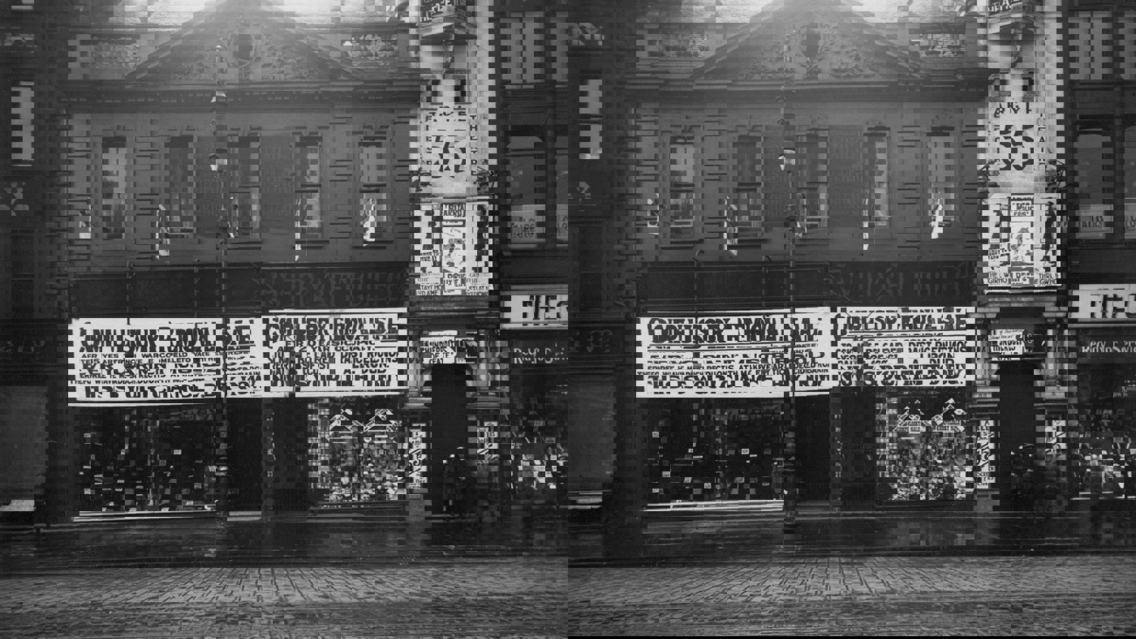 A black and white photograph of Argyle street which has a cobbled road showing a theatre entrance. Other shops have lots of advertisements in their windows.