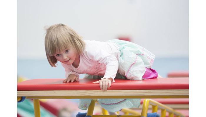 Little girl climbing up on gymnastic equipment 
