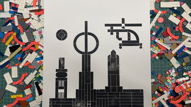 Black prints of buildings and a helicopter on white paper with LEGO blocks on either side of the paper.