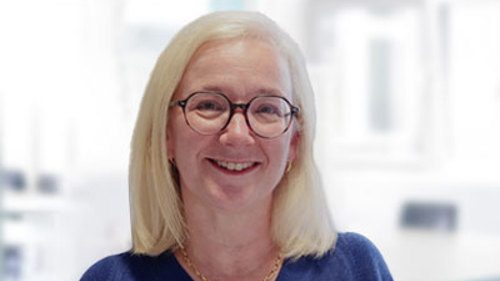 A person with shoulder length blonde hair and round black glasses