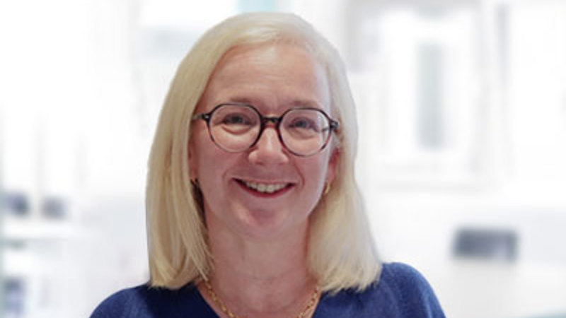 A person with shoulder length blonde hair and round black glasses