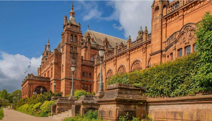 side view of Kelvingrove Art Gallery and Museum with red sandstone bricks against a bright blue sky.