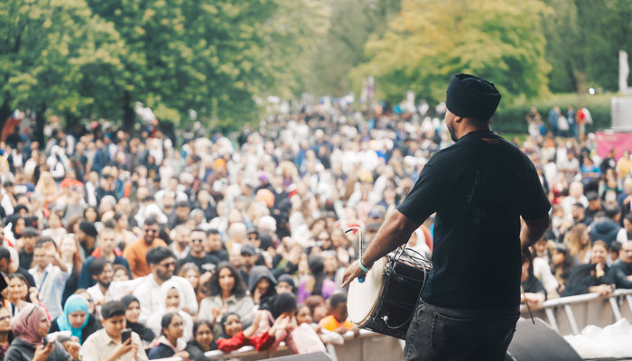 A musician performs in front of a large crowd at an outdoor music festival
