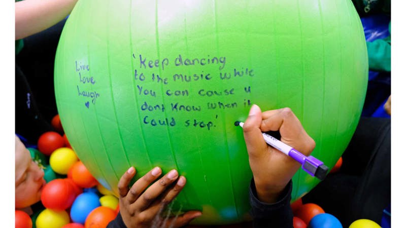 A child write a message on a green yoga ball it reads" Keep dancing to the music while you can, ‘cause you don’t know when it /could stop"