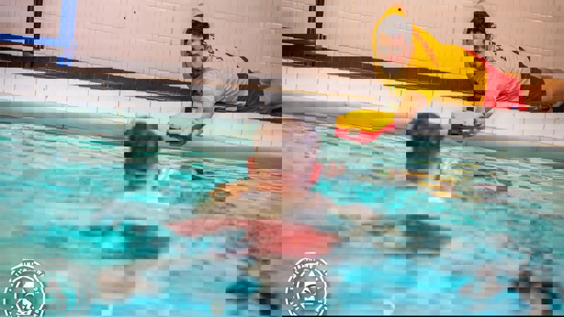 Lifeguard reaching out a float to a person in a swimming pool