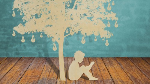 Cut out paper illustration of a young person sitting under a tree reading a book. There are lightbulbs hanging from the tree.