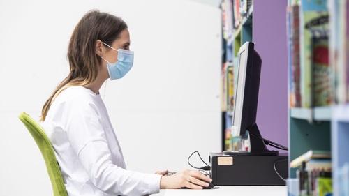 Adult sitting at PC wearing a mask in the library