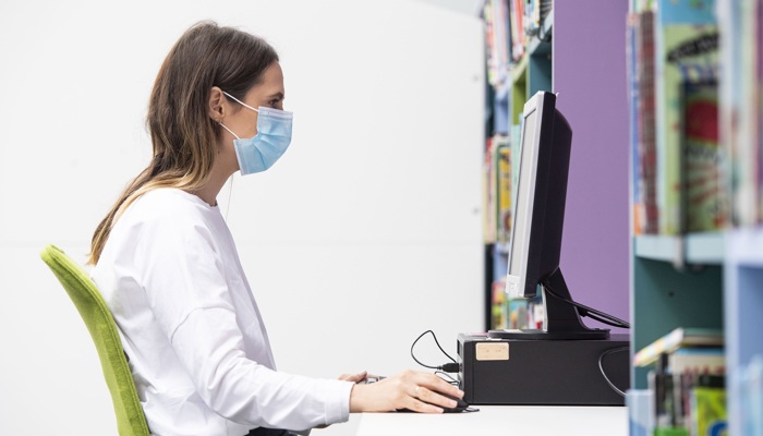 Adult sitting at PC wearing a mask in the library