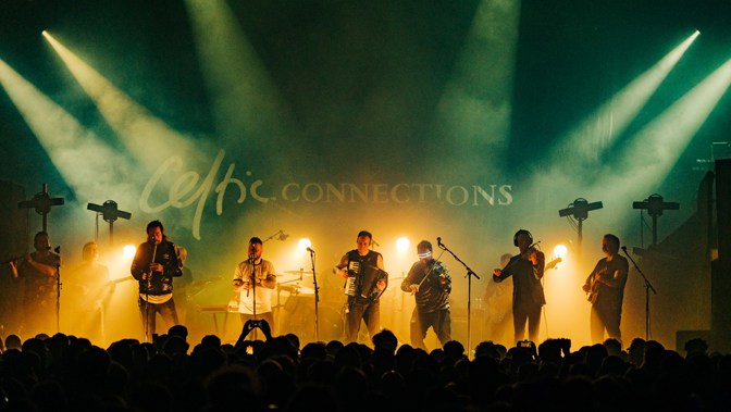 A large band of musicians on a smoky stage playing guitar and violin