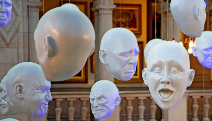 floating head objects suspended from ceiling with different expression in museum gallery setting.