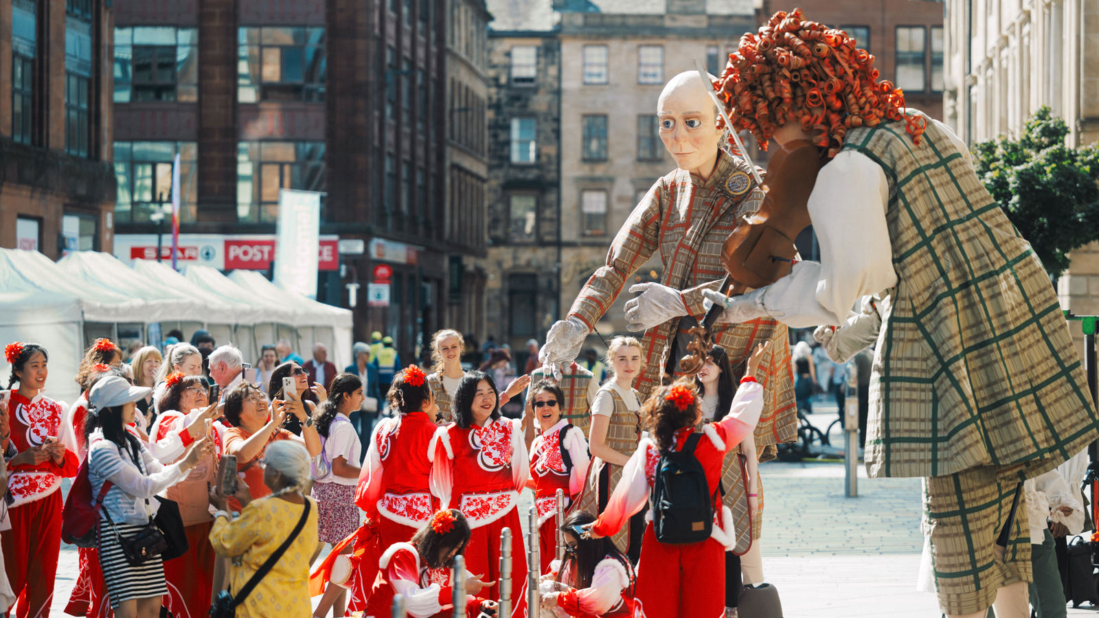 Large street theatre puppets hover over street performers dressed in red costumes