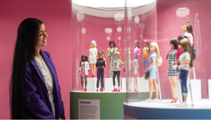 woman with long dark hair looks and smiles at dolls in a large tube
