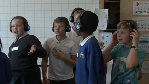 A group of school children dance to music. 
