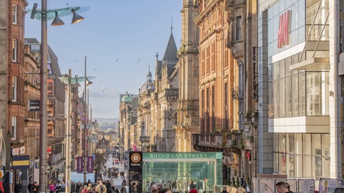 The sun shines on a busy shopping street as people walk up and down