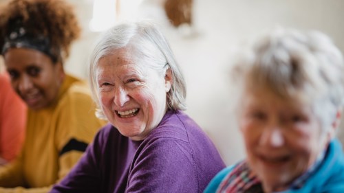 A group of three older adults taking part in a group activity at table and laughing