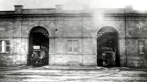 Black and white image of a historical tram depot with two arched entrances with a tram on rails visible through each