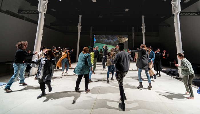 People in multicoloured clothing dance with one another on grey flooring