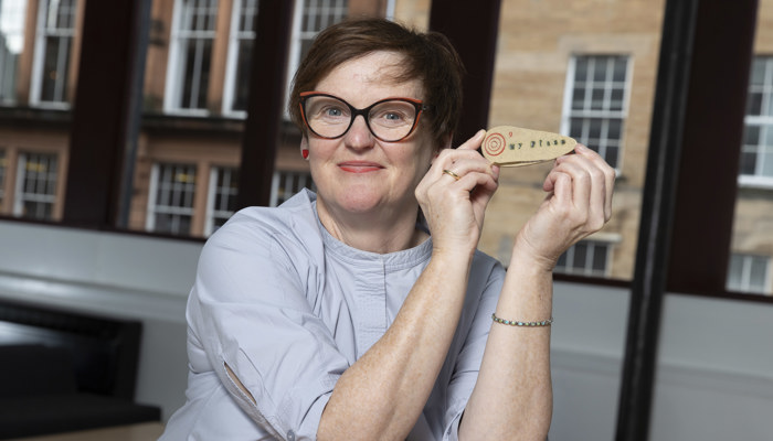 A smiling woman displays a small wooden artwork