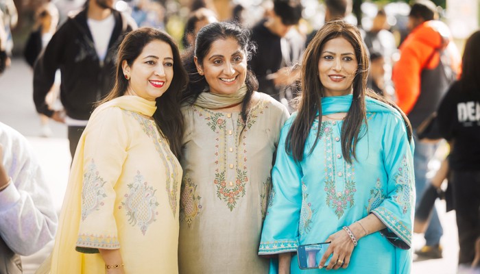 Three people in brightly coloured clothing enjoy themselves at a South Asian festival of music, dance and arts