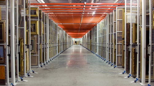 A view down a corridor in the vast painting store at Glasgow Museums Resource Centre with racks of paintings either side
