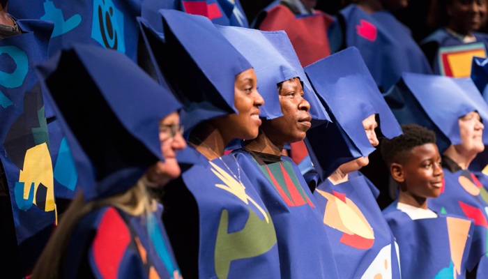 A choir sings, they are wearing creative costumes and hats which are purple.