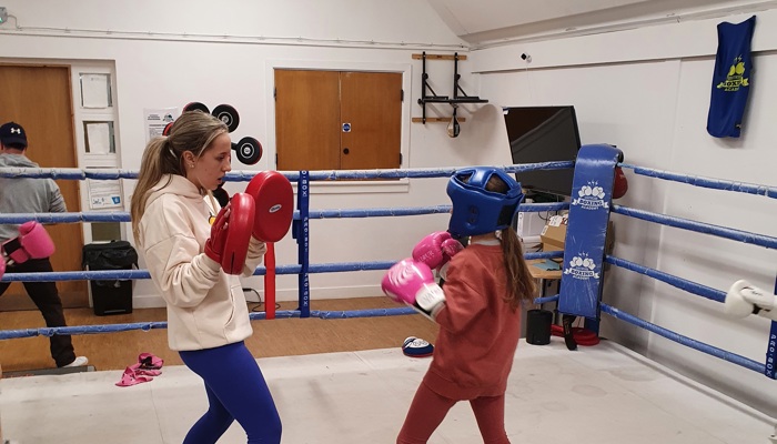 Volunteer holding pads while helping a child box
