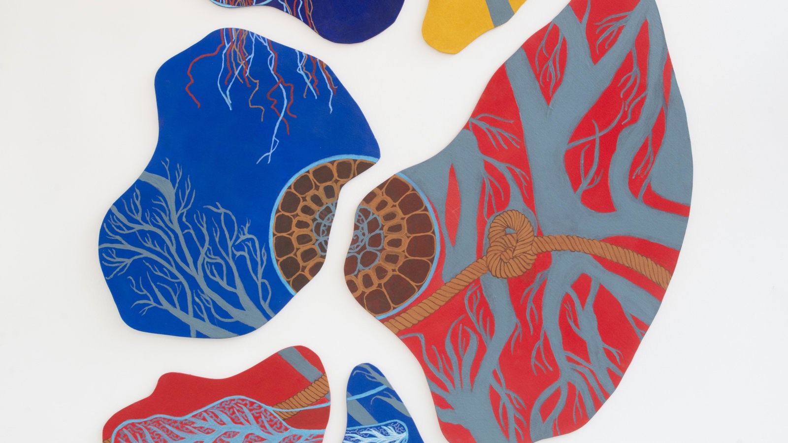 An abstract wall installation made of several irregular, organic‑shaped panels hangs against a white gallery wall. Each panel is filled with intricate patterns that resemble branching vessels, roots, or cellular structures, painted in vivid reds, blues, yellows, and browns. One section features a knot‑like form connected to red branching lines, giving the piece a sense of biological interconnectedness. The overall effect is vibrant, textured, and evocative of natural systems