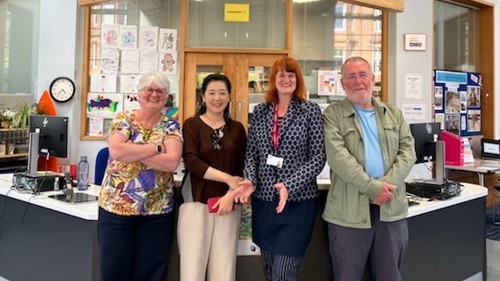 A group of four people are gathered for a photograph in front of a reception desk at a library