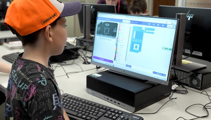 Young person using block-based coding software on a desktop computer in a library.