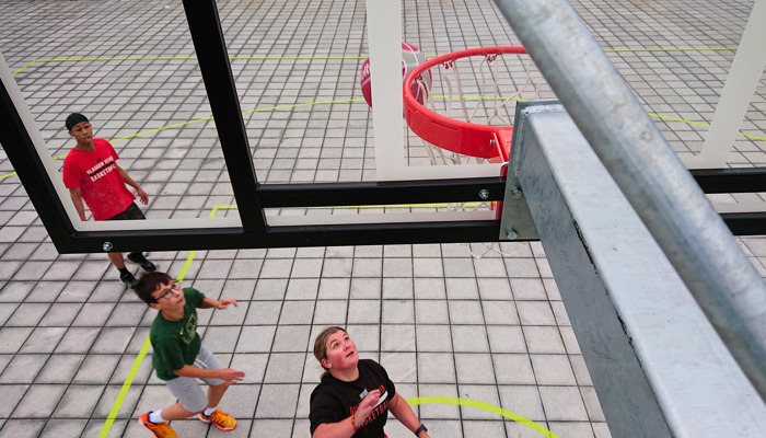  Three young people play basketball on an outdoor court at Riverside Museum, viewed from below the hoop.