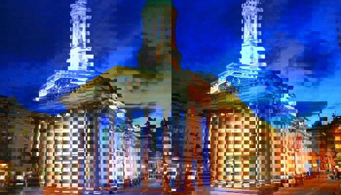 night exterior shot of GoMA showing the classical frontage illuminated by spotlights and a blue sky above