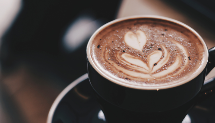close up of a ceramic black cup and saucer containing a drink topped with latte art.