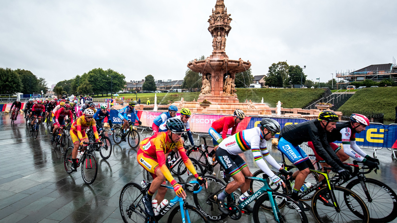 A group of cyclists in multi-coloured racing gear cycle past an ornate 