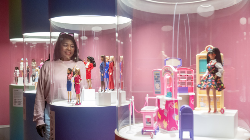 Woman looks at Barbie dolls in glass display case and smiles