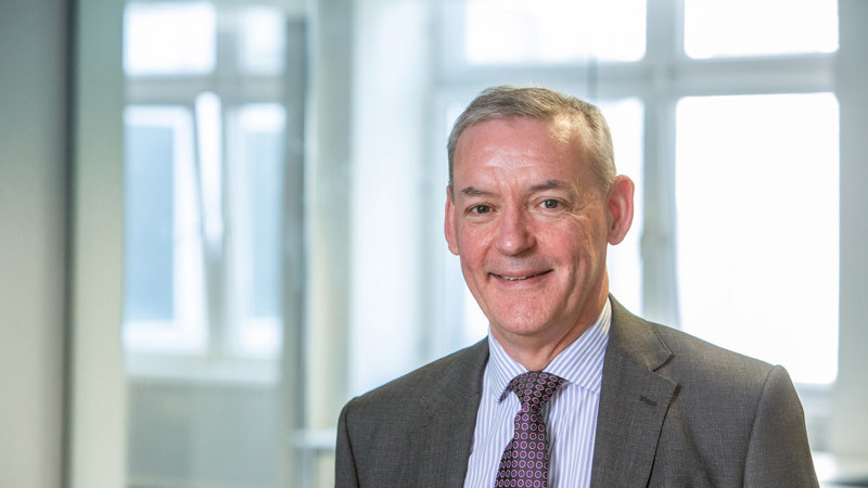An image of a man in a suit against a backdrop of windows