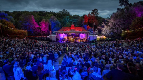 A large crown enjoying a concert in the evening at an outdoor bandstand
