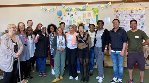 A large group of people gathered for a photo in front of a colourful display of artwork under a banner that reads Adult Learning Week