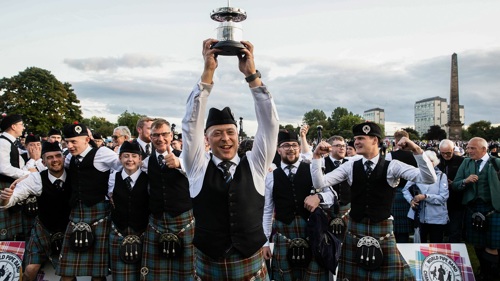A large group of people in kilts celebrating and holding a trophy in the air