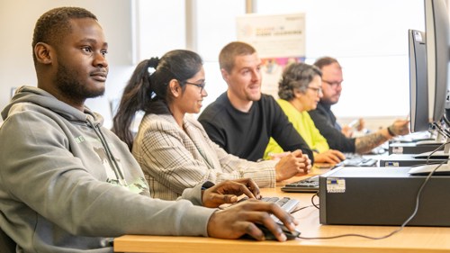 A group of five people sitting at a bank of computers in a library. They appear to be working together